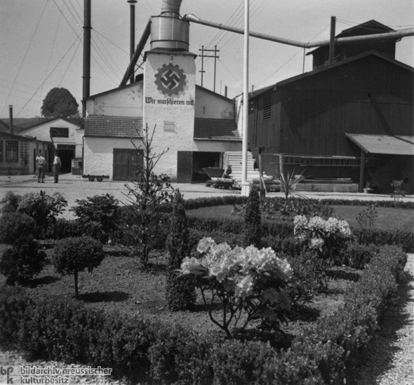 „Musterbetriebshof” mit Wandparole der Deutschen Arbeitsfront: „Wir marschieren mit” (1937/38)